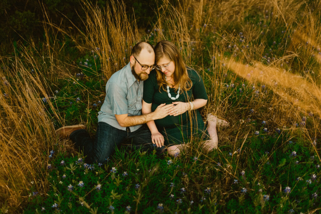 Couple sitting in grassy field, woman pregnant.