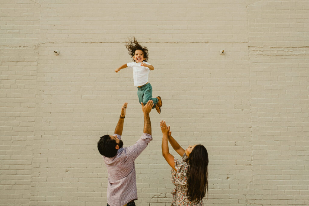 Parents lift happy child in the air outside.