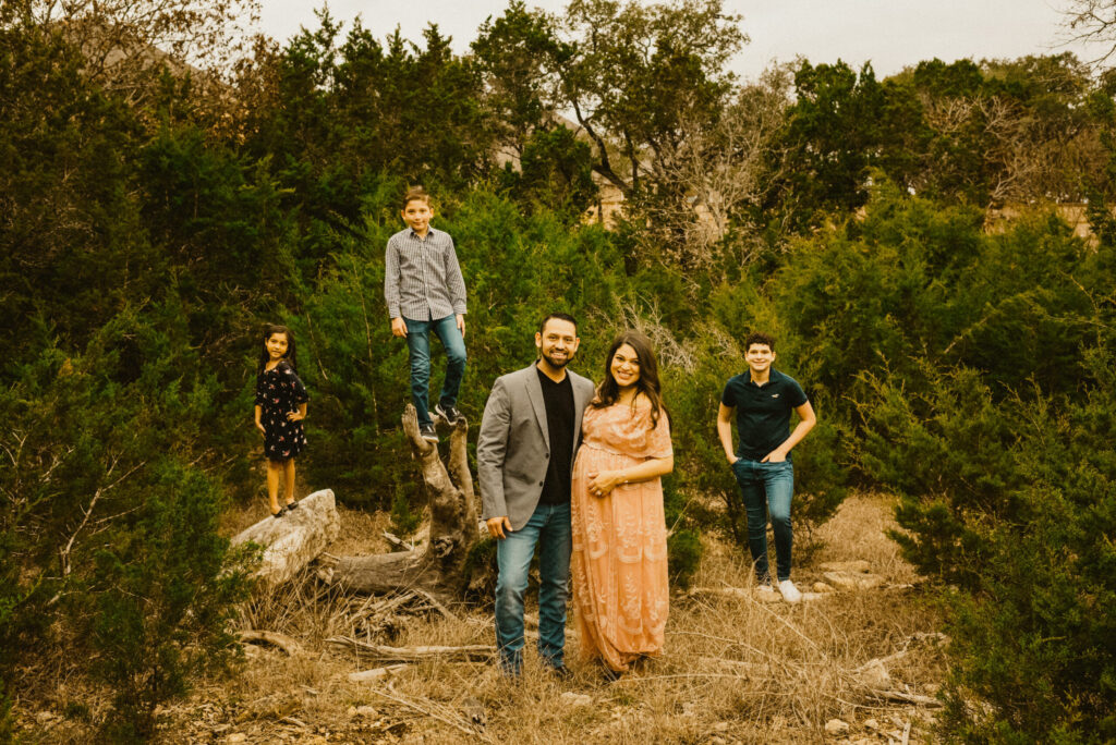 Family posing outdoors among trees and grass.