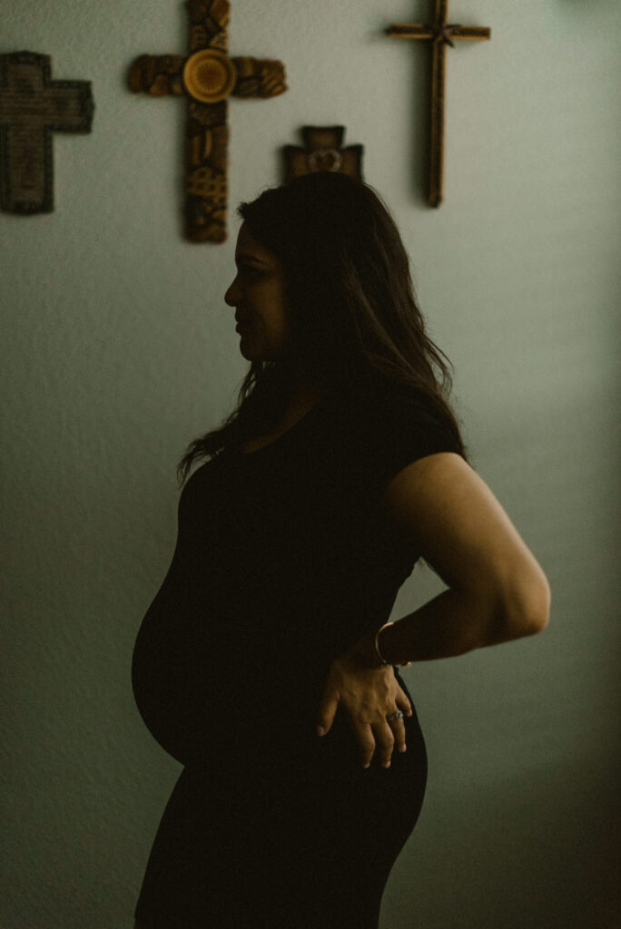 Pregnant woman silhouette with wall crosses backdrop.