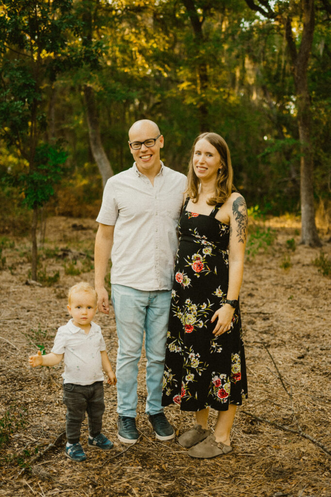 Family posing outdoors in a wooded area.