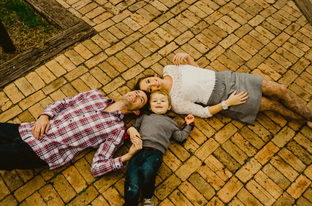 Family lying on brick path, smiling together.