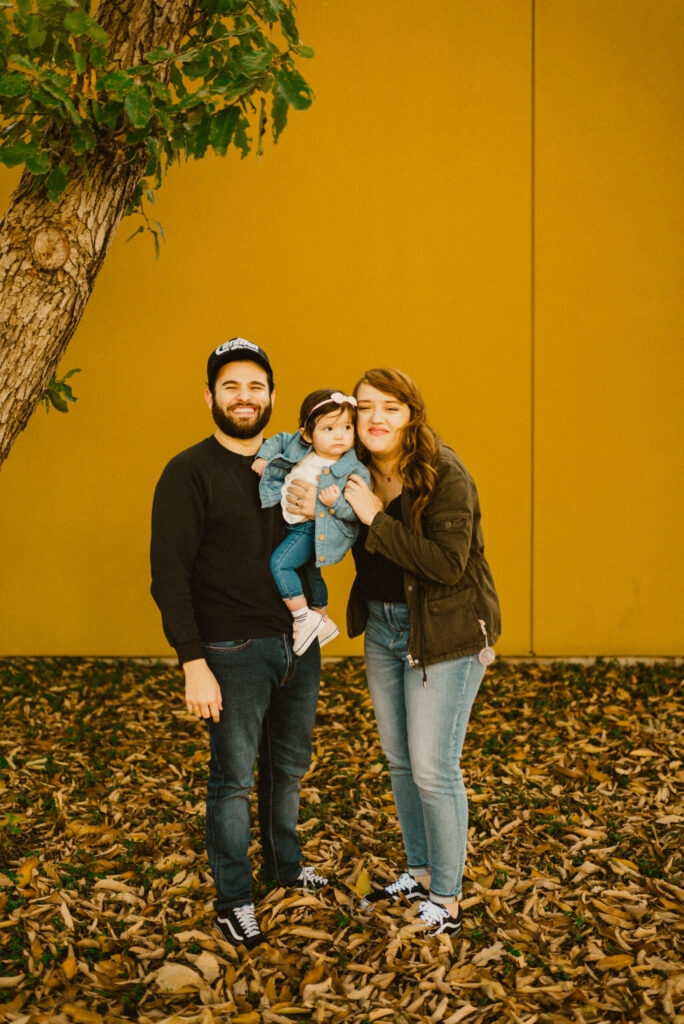 Family posing in front of yellow wall with leaves.