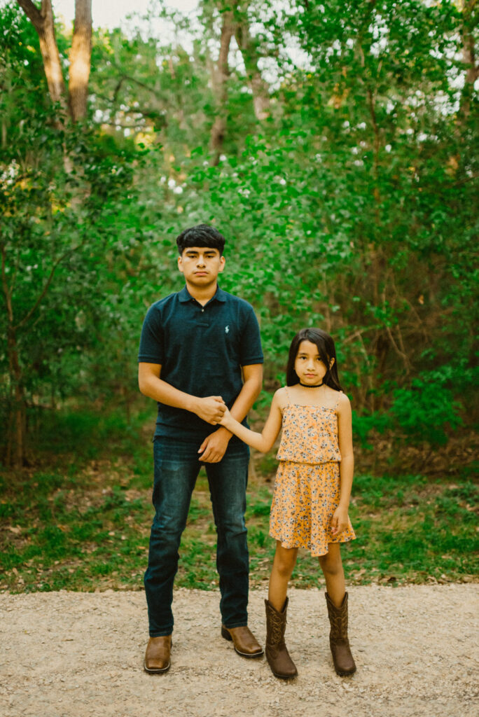 Siblings holding hands in a green forest.