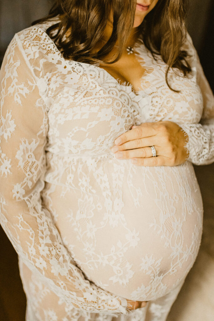 Pregnant woman in lace dress holds her belly.