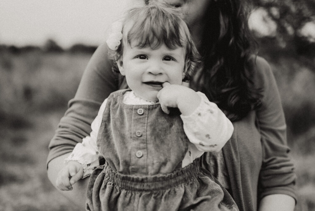 Smiling toddler in mother's arms outdoors.