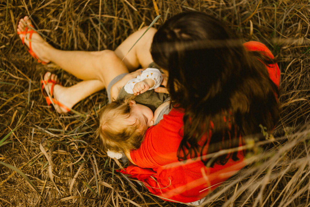 Mother breastfeeding baby outdoors on dry grass.
