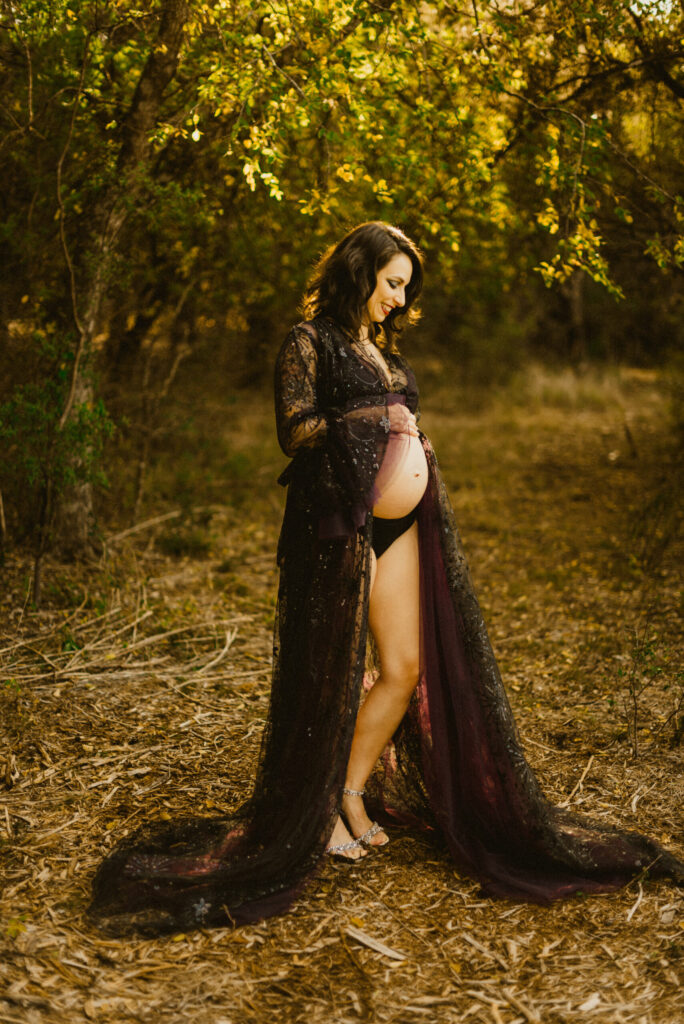 Pregnant woman in lace robe in forest setting.