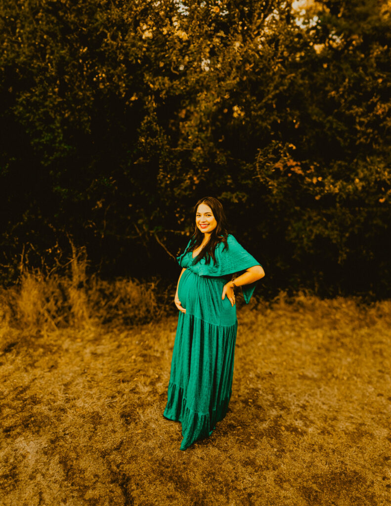 Pregnant woman in green dress standing outdoors smiling.