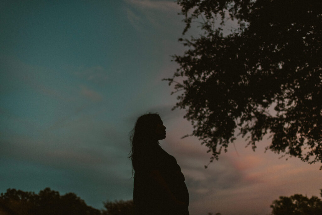 Silhouette of person at sunset, tree in foreground.