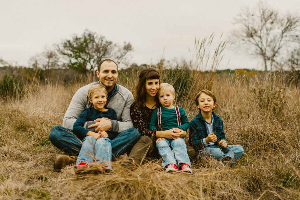 Family sitting in grassy field, smiling together.