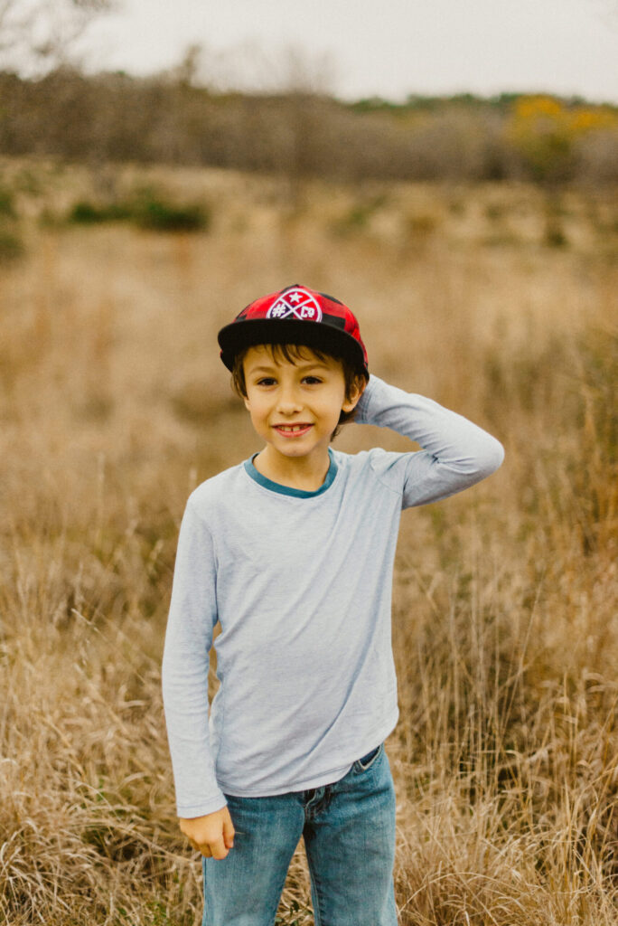 Child smiling outdoors wearing cap and jeans.