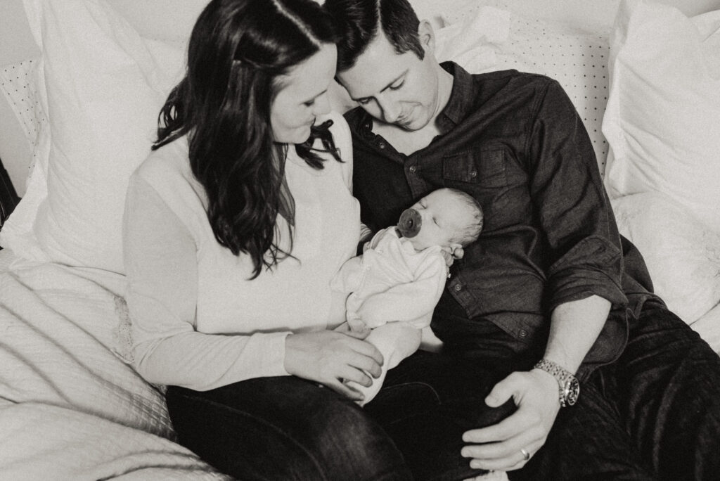 Parents lovingly cradle newborn on bed.