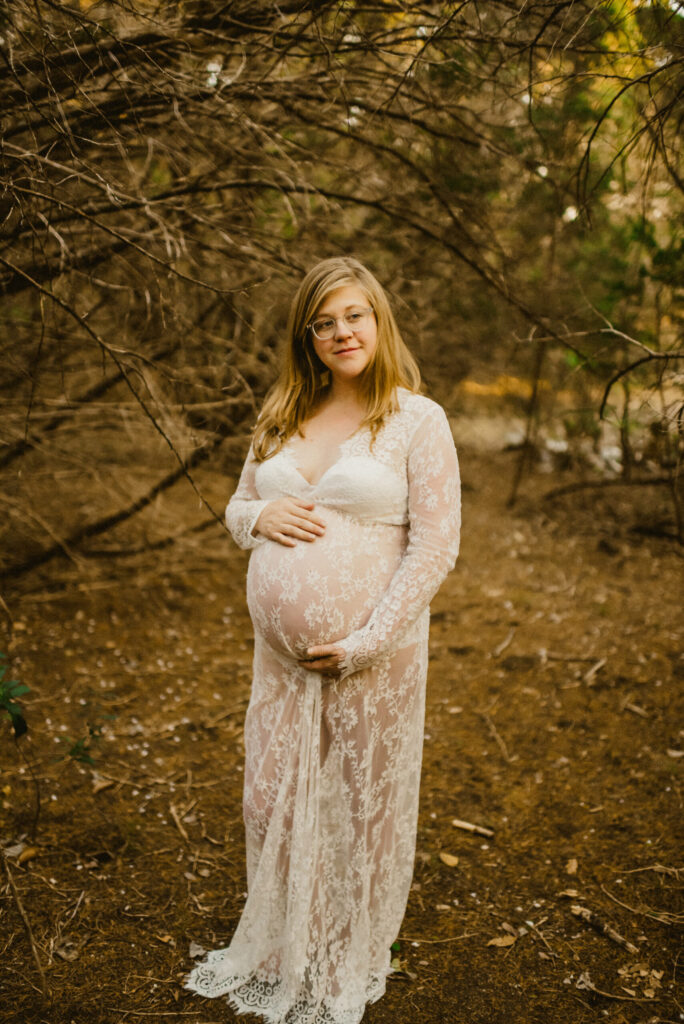 Pregnant woman in forest wearing lace dress.