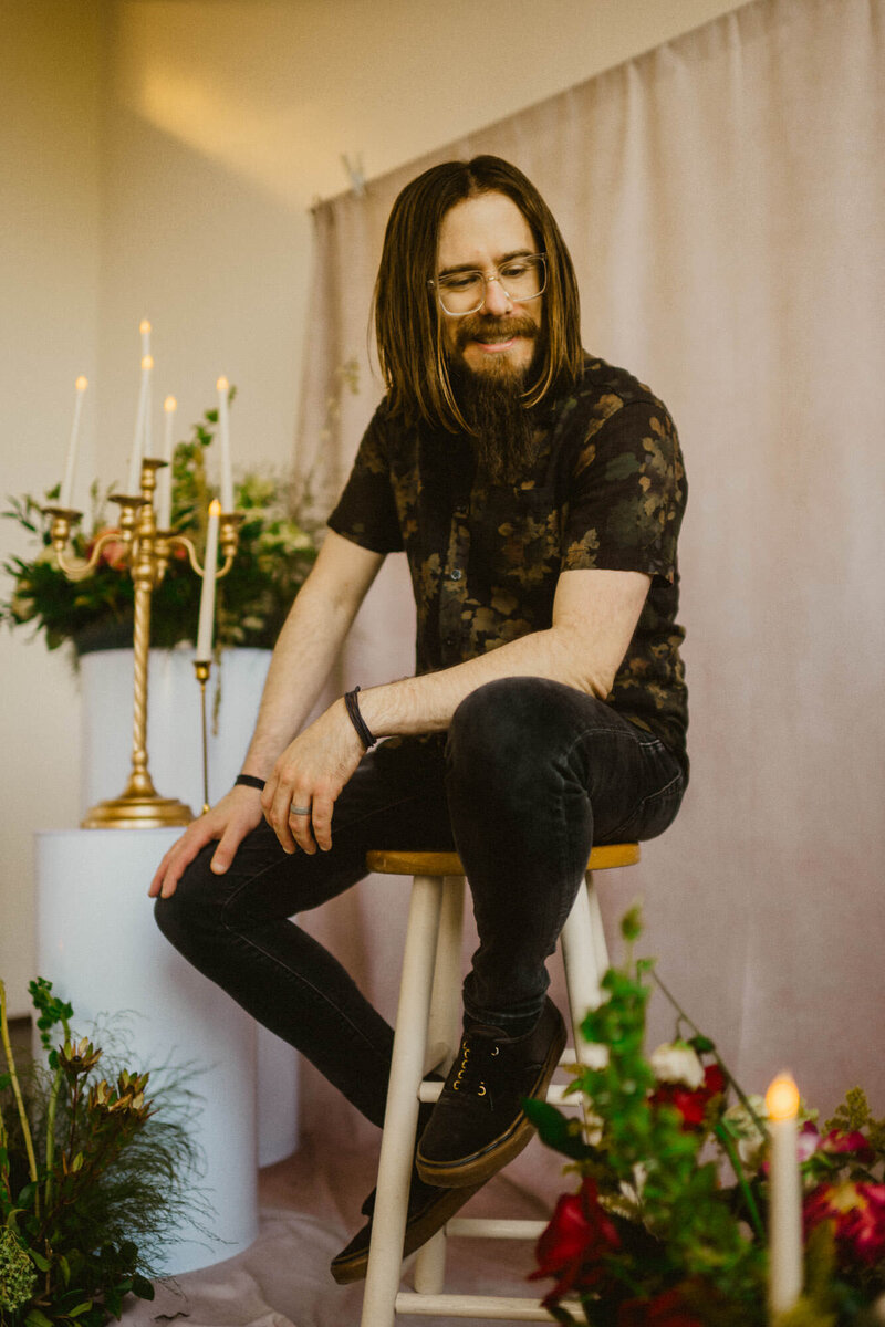 Man with long hair sitting among candles and flowers